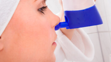 Nasendusche: Eine junge Frau hält eine blau-weiße Nasendusche an die Nase.